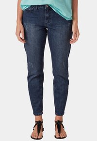 Tumman väriset, slim-fit farkut, joissa on hienovaraista kulutusta. Keskikorkea vyötärö ja kapenevat lahkeet. Yhdistetty mustiin, remmillä varustettuihin sandaaleihin.