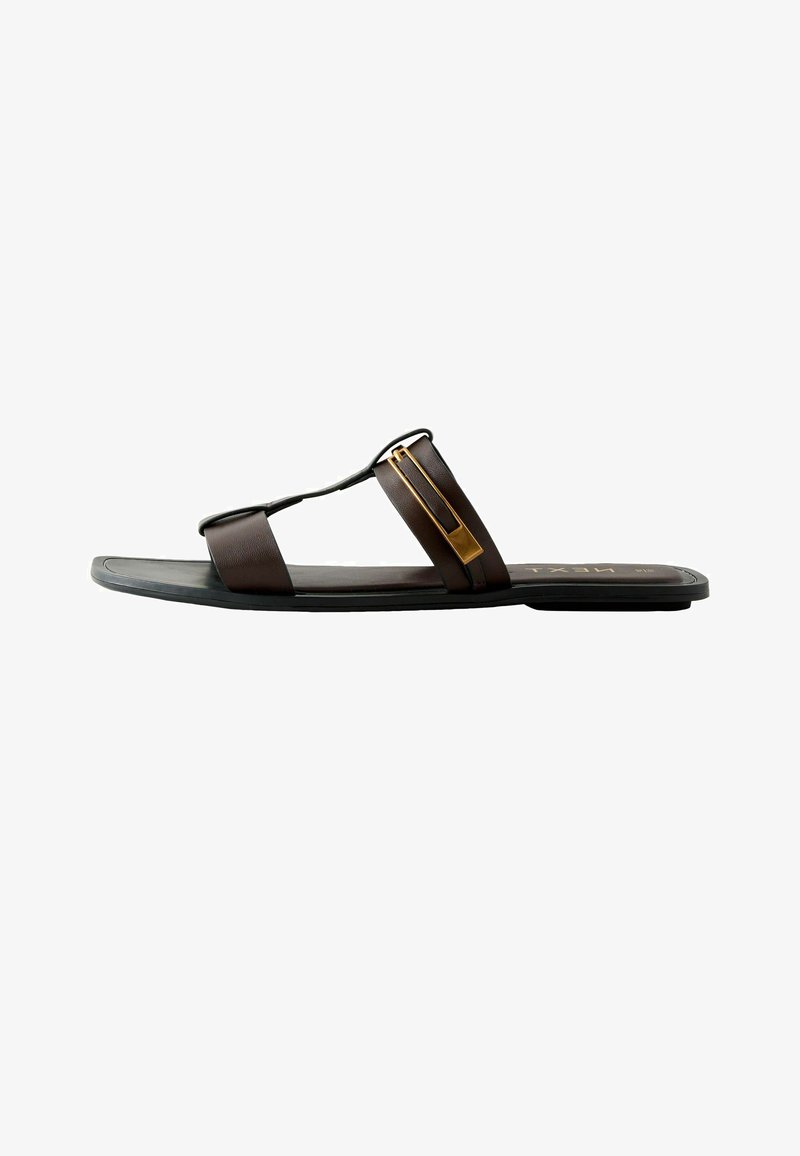 Sandale plate pour homme avec semelle noire, brides en cuir brun foncé et détail boucle en métal doré sur fond blanc.