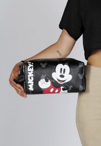 Trousse de maquillage noire avec un design imprimé de Mickey Mouse, accents rouges, surface texturée et une poignée latérale pour un transport facile.