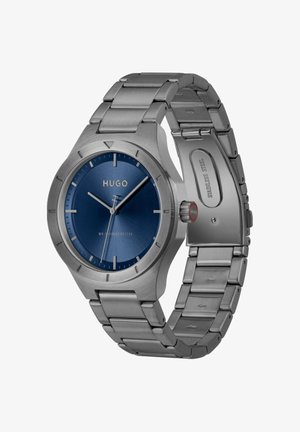 Montre-bracelet en acier inoxydable avec cadran bleu, index argentés, trois aiguilles et bracelet à maillons métalliques ouvert.