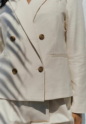 Beige graue Doppelreiher-Blazer aus strukturiertem Stoff, mit zwei vorderen Taschen und braunen Knöpfen zum Schließen, in taillierter Form.