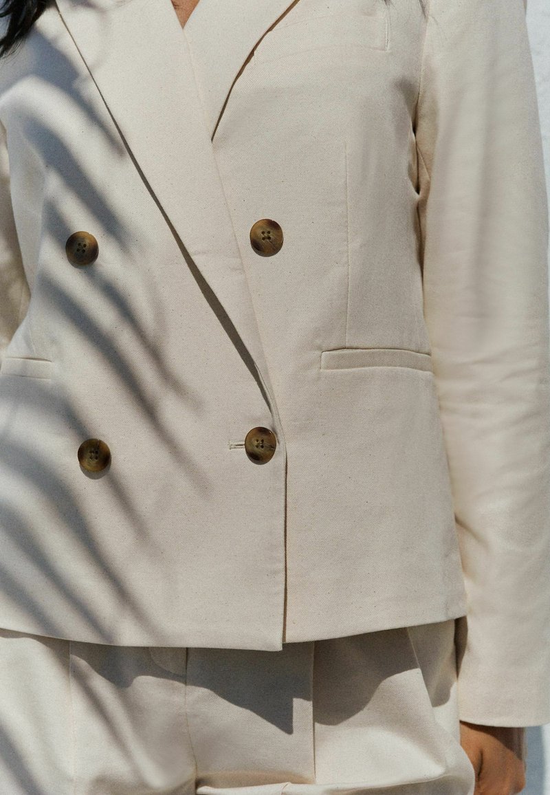 Beige double-breasted blazer van gestructureerde stof, met twee voorzakken en beige knopen voor de sluiting, in een getailleerde pasvorm.