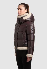Giubbotto imbottito di un borgogna scuro con cappuccio, dotato di un colletto e bordi in pelliccia sintetica beige, materiale esterno lucido e chiusura con zip frontale.