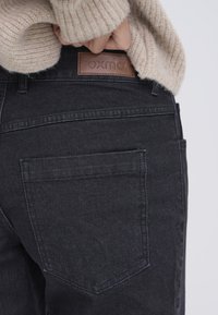 Black jeans with a textured fabric, featuring a leather patch with embossed "oxmo" logo at the back waistband and a back pocket.