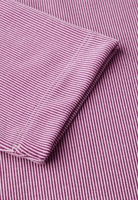 Tessuto di cotone con strisce sottili bianche e rosa scuro alternate, caratterizzato da un colletto piegato con cuciture ordinate. Texture morbida e finitura liscia.