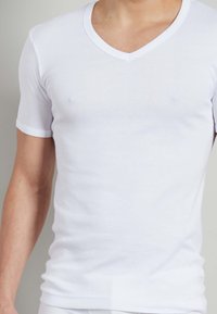 T-shirt Bianca in cotone con scollo a V, maniche corte, design aderente e texture morbida. Dettagli minimi con cuciture rinforzate.