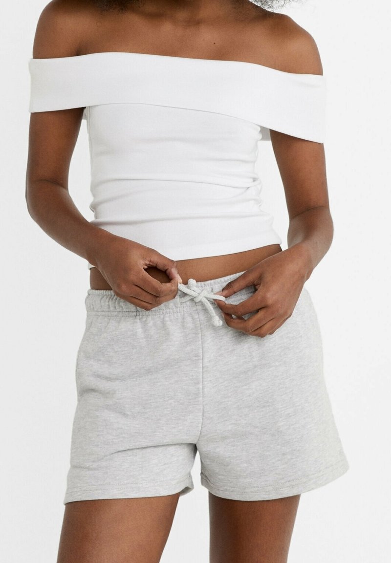 Witte off-shoulder top met een fitted ontwerp; grijze shorts met elastische tailleband en drawstring, zachte textuur en casual stijl.