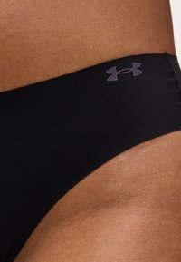 Κοντινή λήψη της λεκάνης ενός ατόμου που φορά μαύρο κάτω μέρος μαγιό Under Armour με το λογότυπο Under Armour στη ζώνη μέσης.