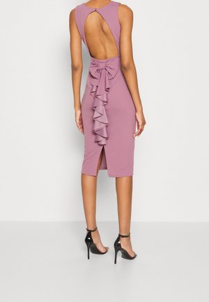 Back view of woman wearing a sleeveless mauve midi dress with a large bow and cascading ruffles down the open-back center, paired with black heels.