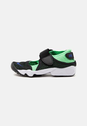 Baskets Nike noires et vertes avec tige en mesh, semelle blanche, logo bleu sur l’orteil et le talon, et bride noire réglable autour de la cheville.