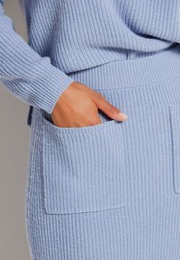 Hellblaue, gerippte Strickjacke mit lockerer Passform. Sie verfügt über lange Ärmel und eine Fronttasche im Rock, die ein strukturiertes Strickmuster zeigt.