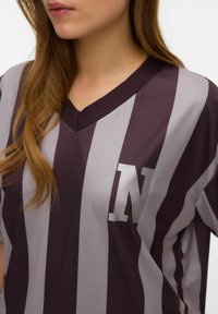 Tumepruunide ja hallide triipudega spordipluus V-kaelusega ning vasakul rinnal metallik-hall "N" logoga. Pehme, hingav materjal.