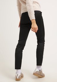 Pantalons ajustés noirs en denim avec une texture lisse, associés à des chaussures gris clair ornées d'accents blancs et à des chaussettes grises.