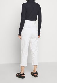 Zwarte geribbelde lange mouwtop in combinatie met witte high-waisted broek. De broek heeft een rechte snit en is iets cropped bij de enkel.