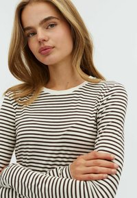 Striped long-sleeve top in cream and dark brown. Features a round neckline and soft fabric, with narrow horizontal lines throughout.