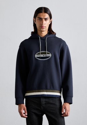 Felpa in cotone blu navy con logo ricamato, cordino regolabile e orlo testurizzato con strisce verdi, bianche e blu nella parte inferiore.
