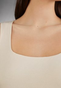 Lichtbeige tanktop met een brede ronde halslijn, een gladde textuur en een aansluitend ontwerp, met minimale stiksels en geen zichtbare hardware.