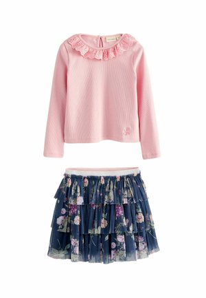 Lyserød bluse med lange ærmer, prydet med en flæset blondekrave og broderet blad. Marineblå nederdel med blomsterdesign og lag, der har elastisk talje.
