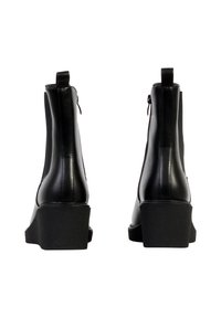 Paire de bottines noires à talons épais, avec des boucles à l'arrière et une tige en cuir, vues de dos sur un fond blanc.