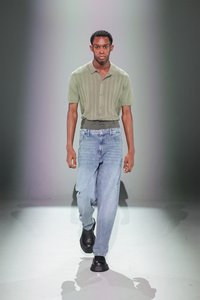 Tricou polo verde cu rigidă, blugi bleu deschis și cizme negre masive. Tricoul are un decolteu cu butoni și este ajustat la talie.