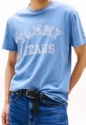Jasnoniebieski bawełniany t-shirt z białym napisem "TOMMY JEANS". Krótkie rękawy i okrągły dekolt, zestawiony z ciemnoniebieskimi dżinsami i czarnym plecionym paskiem.