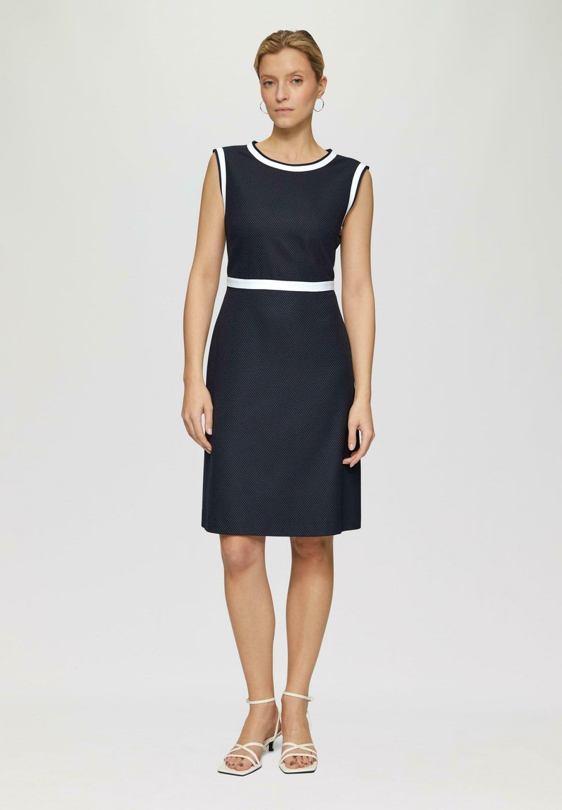 Robe sans manches marine avec une accentuation blanche à la taille et au col, dotée d'un tissu texturé et d'une coupe mi-longue.
