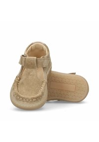 Tan suède schoenen met een gestikt moccasin ontwerp, verstelbare band en een flexibele rubberen zool. Ronde neus en minimalistische details.