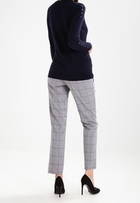 Marint stickad tröja med långa ärmar, med sidofickor, kombinerad med grå rutiga byxor och svarta stilettklackar.