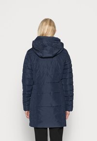 Marinblå puffjacka med huva, med kviltad textur och en åtsittande midjedesign, visad bakifrån.