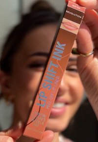 Lip Shift Ink läppennas förpackning i persikofärg med blå text; har etiketten "Peel Off Lip Liner" och en läppgrafik.