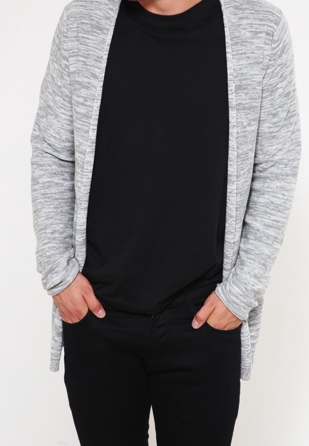 Grå, texturerad cardigan med öppen front, som bärs över en svart t-shirt och svarta byxor. Cardiganen har långa ärmar och en avslappnad passform.