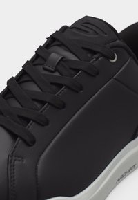 Mustad tenniskingad matt viimistlusega, mustad lamedad paelad, õmmeldud paneelid ja valge tallaga, mille külgedel on "ADVANT" bränding.