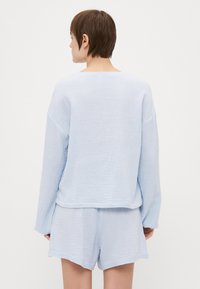 Lys blå, tekstureret bomulds loungetøjssæt med en løs langærmet top og matchende shorts. Minimalistisk design med en afslappet form.