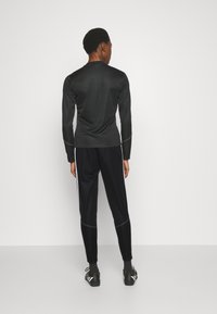 Čierne športové tričko s dlhými rukávmi a okrúhlym výstrihom, v kombinácii s čiernymi nohavicami s bielymi pruhmi po boku. Obe položky sú priliehavé a hladké na dotyk.