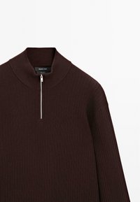 Burgunderfarbener gerippter Pullover mit hohem Kragen und halbem Reißverschluss. Weiche Textur mit lässiger Passform und überschnittenen Schultern.