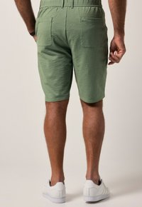 Pantalones cortos verdes con textura y un patrón a cuadros, dos bolsillos traseros y un corte relajado. Combinados con zapatillas blancas.