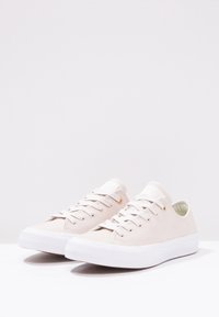 Baskets en toile beige avec semelle en caoutchouc blanc, bout rond, fermeture à lacets, œillets dorés et surface texturée.