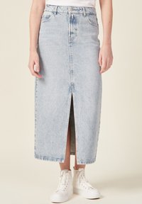 Gonna di jeans azzurra chiara con uno spacco davanti, di lunghezza media, con texture sbiadita e design a cinque tasche, abbinata a sneakers bianche alte.