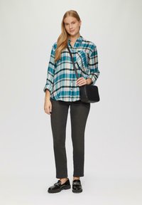 Karierte Hemd mit blauem, schwarzem und weißem Muster; Knöpfe an der Vorderseite. Kombiniert mit schwarzen Skinny Jeans und schwarzen Loafers. Die Umhängetasche hat eine strukturierte Oberfläche.