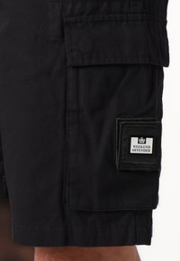 Shorts cargo noirs en coton avec une finition texturée. Comprend une poche latérale avec un patch carré portant l'inscription "WEEKEND OFFENDER."