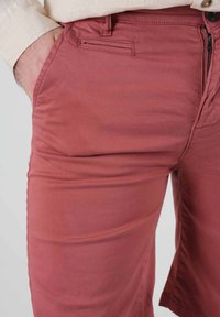 Des shorts en mélange de coton de couleur rose poussiéreux présentent une poche latérale, une fermeture éclair avec bouton, et un tissu texturé pour le confort.