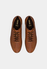 Καφέ δερμάτινα αθλητικά παπούτσια με μαύρα κορδόνια, με ομαλή υφή, στρογγυλεμένη μύτη και διακριτικές λεπτομέρειες ραφών. Διακριτική σήμανση Geox στο εσωτερικό.