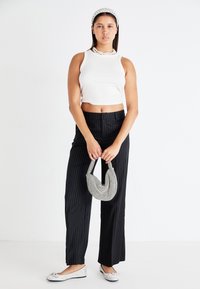 White ribbed crop top, black pinstriped wide-leg trousers, silver flat shoes with bows, and a houndstooth-patterned mini bag.