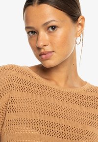 Light brown knit sweater featuring a textured pattern with open crochet stripes and a ribbed neckline. Short sleeves and a relaxed fit.