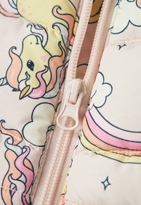 Vatteret jakke i et blødt pastelrosa stof med mønstre af enhjørninger og skyer. En lysefarvet lynlås er synlig.