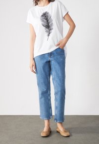 Camiseta blanca con gráfico de pluma negra, jeans de pierna recta azul y bailarinas beige. Tela de algodón suave con mangas cortas y corte relajado.