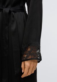 Čierny saténový župan s čipkou na manžete. Čipka má kvetinový vzor, ktorý zvýrazňuje eleganciu župana. Súčasťou je zodpovedajúci opasok.