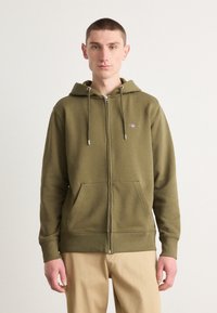 Olijfgroene hoodie met rits gemaakt van zachte stof, met een voorkant rits, een capuchon met trekkoord en twee voorzakken. Eenvoudig geborduurd logo.