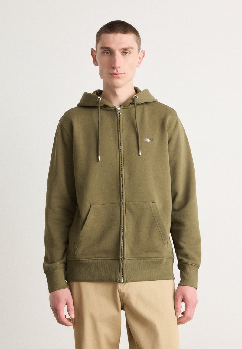 Olijfgroene hoodie met rits gemaakt van zachte stof, met een voorkant rits, een capuchon met trekkoord en twee voorzakken. Eenvoudig geborduurd logo.