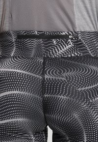 Leggings de patrón negro y gris que cuentan con un bolsillo con cremallera, textura suave y contornos diseñados para ajustarse al cuerpo.